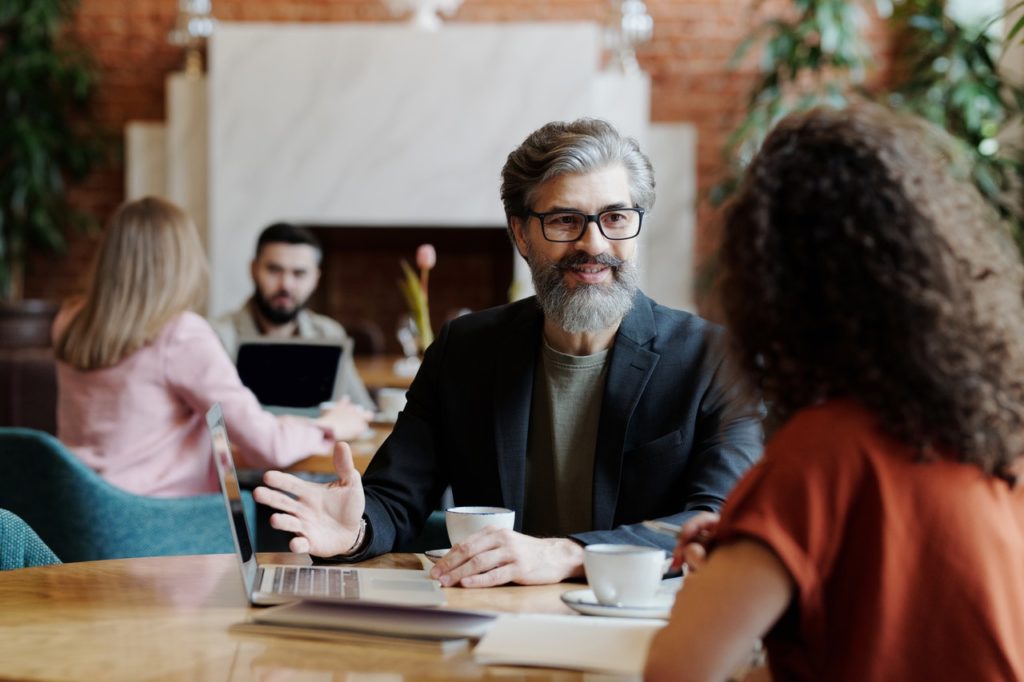 bearded man talking to a woman in a coffee shop