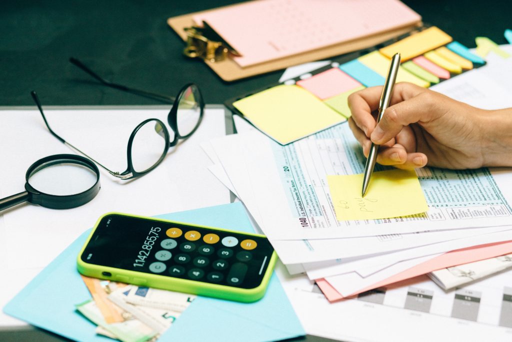 glasses, magnifying glass, calculator, tax documentation and hand with a pencil