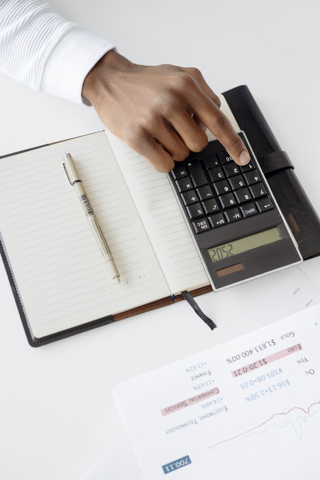 man typing on calculator atop day planner